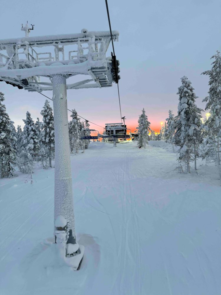 A frosted chairlift tower over a groomed slope, with orange light low behind the trees
