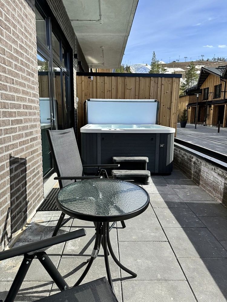 The terrace on a sunny day, with the hot tub, a glass table and chairs